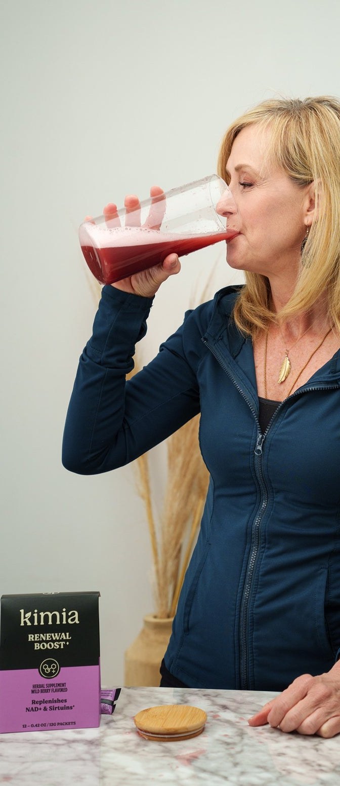 A woman drinking a glass of the wild-berry renewal blend at her kitchen counter